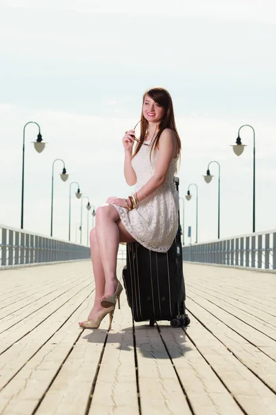 Kvinnan sitter på resväska, pier i bakgrunden — Stockfoto