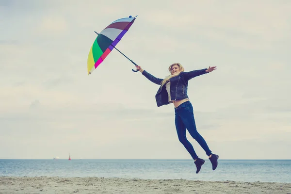 Woman jumping with colorful umbrella on beach — Stock Photo, Image
