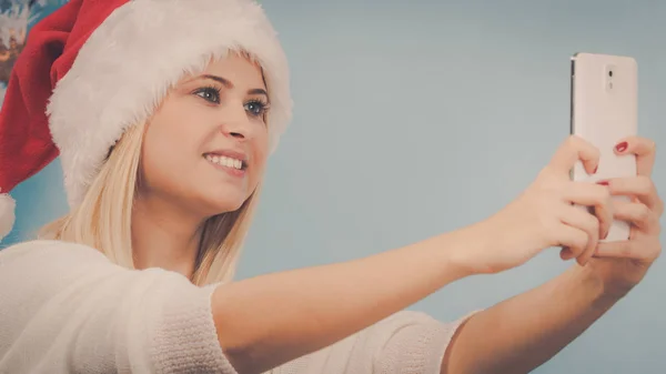 Girl in santa hat taking picture of herself using phone — Stock Photo, Image