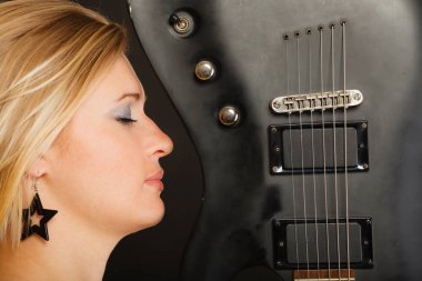 Elektro gitar tutan sarışın kadın, siyah arkaplan.