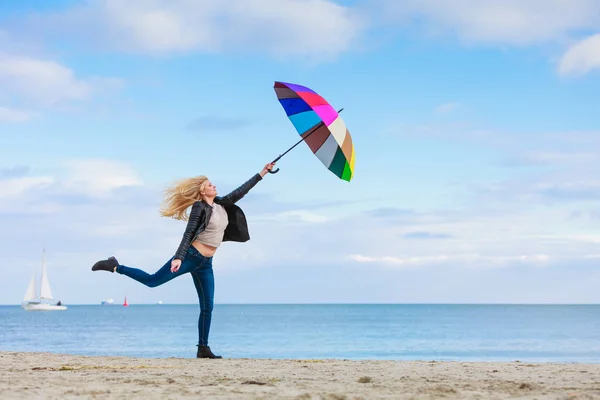 Woman jumping with colorful umbrella on beach