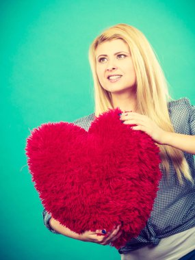 Kırmızı yastık kalp şeklinde tutan mutlu kadın