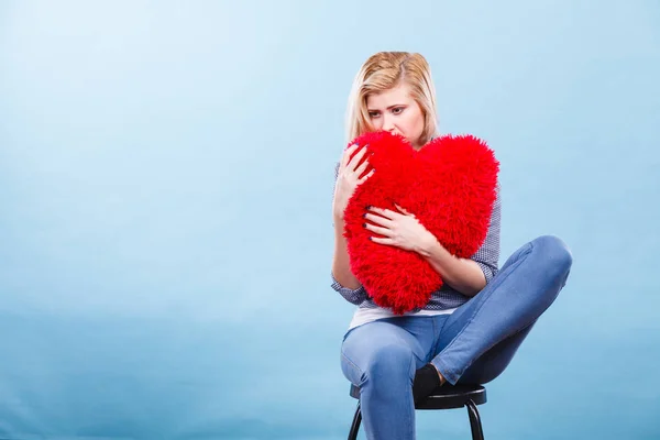 Λυπημένη γυναίκα κρατώντας κόκκινο μαξιλάρι σε σχήμα καρδιάς — Φωτογραφία Αρχείου