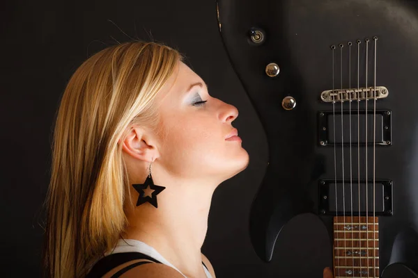 Blondynka trzyma gitarę elektryczną, czarne tło — Zdjęcie stockowe