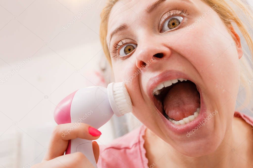 Shocked woman using facial cleansing brush