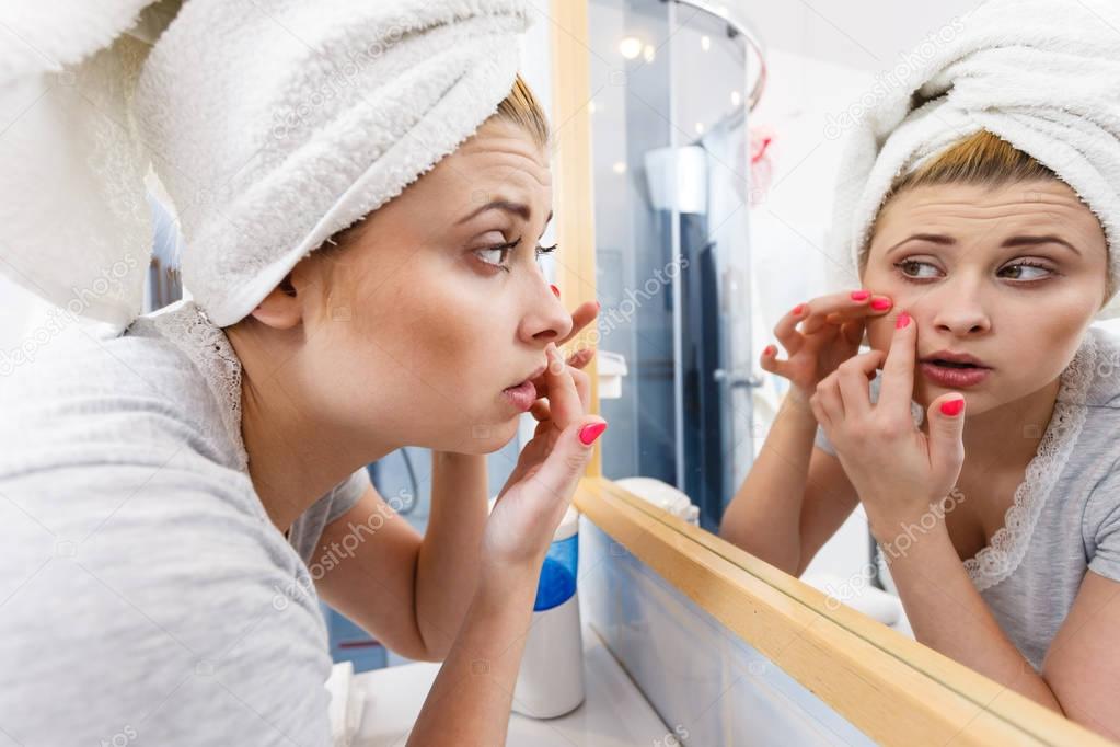 Woman looking in mirror dealing with acne