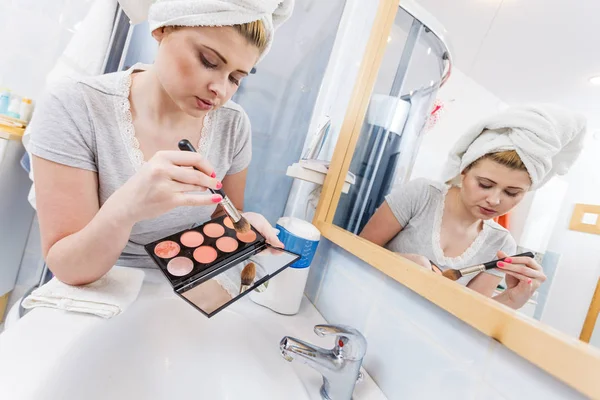 Woman in bathroom applying contour bronzer on brush