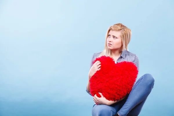 Kırmızı yastık kalp şeklinde tutan üzgün kadın — Stok fotoğraf