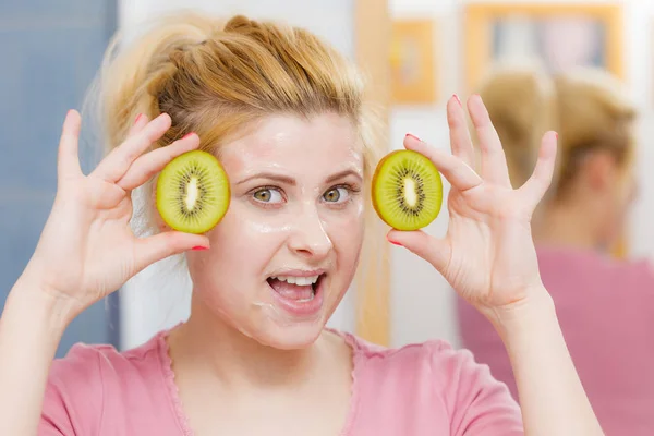 Vrouw met gel masker op het gezicht bedrijf kiwi — Stockfoto