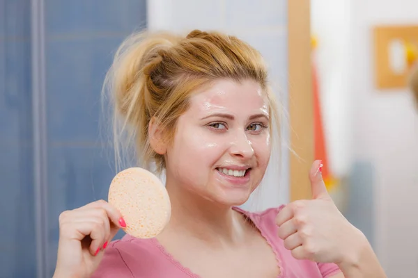 Woman having wash gel on face holding sponge