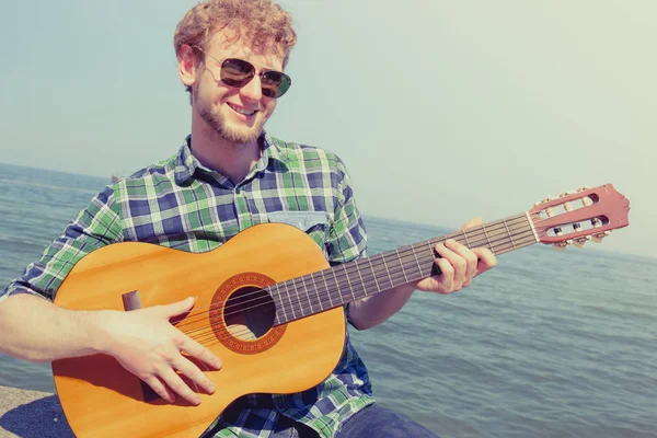 Jonge man hipster gitaarspelen door zee oceaan. — Stockfoto