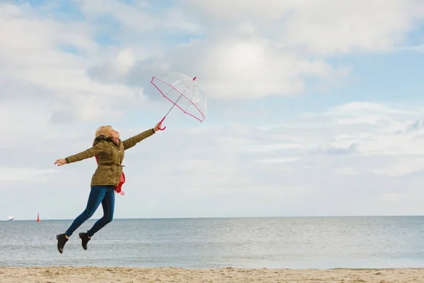 Kobieta, skoki z przezroczystym parasol na plaży — Zdjęcie stockowe