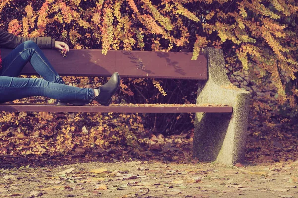 Pernas de mulher sentado no banco no parque outonal — Fotografia de Stock