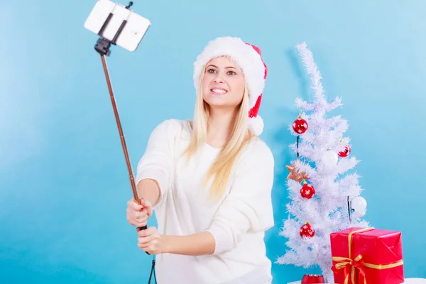 Dziewczyna w santa hat biorąc obraz siebie za pomocą selfie stick — Zdjęcie stockowe