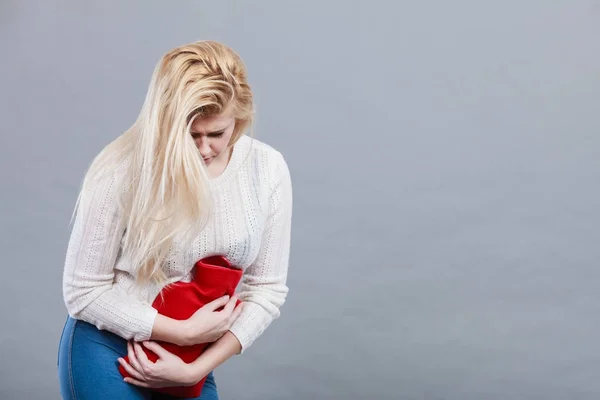 Femme sentiment crampes d'estomac tenant une bouteille d'eau chaude — Photo