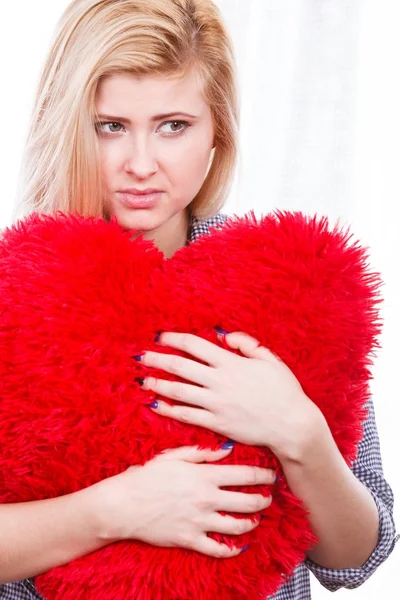 Sad woman holding red pillow in heart shape — Stock Photo, Image