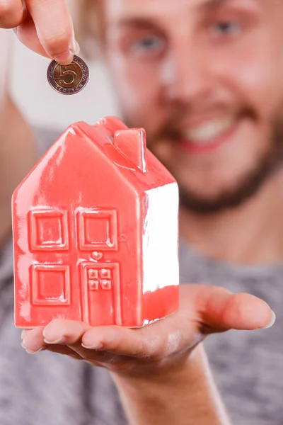 Man putting money into house piggybank