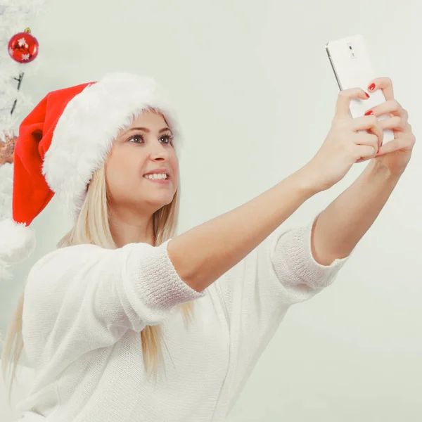 Girl in santa hat taking picture of herself using phone — Stock Photo, Image