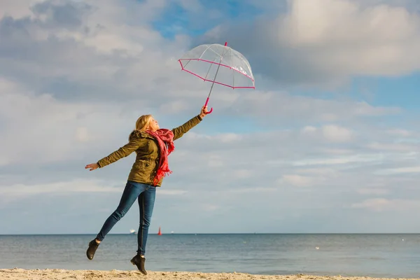 Kobieta, skoki z przezroczystym parasol na plaży — Zdjęcie stockowe