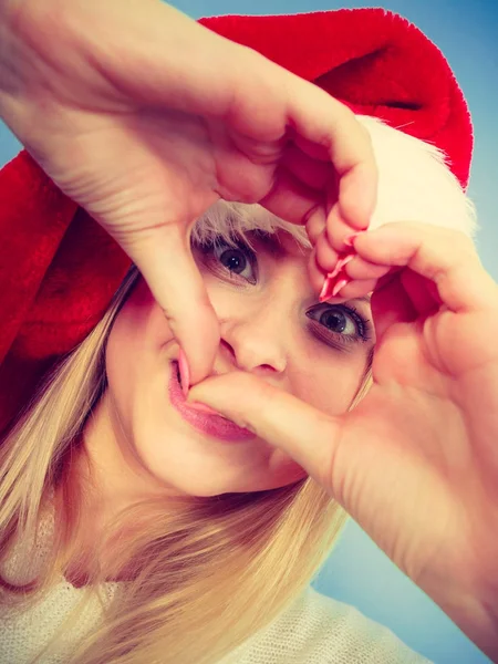 Girl in santa claus hat making heart symbol with fingers — Stock Photo, Image