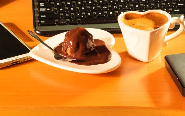 Cup of coffee and chocolate cake next to computer. — Stock Photo, Image