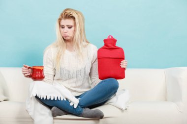 Sıcak su şişesi ve çay Kupası tutan kadın