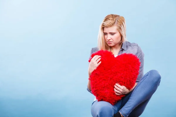 Mujer triste sosteniendo almohada roja en forma de corazón — Foto de Stock