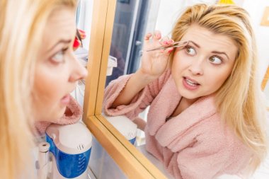 Kaşlarını cımbızla temizleyen kadın.