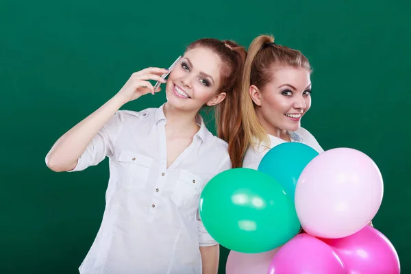 Duas meninas com telefone celular e balões — Fotografia de Stock