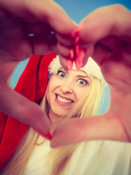 Menina em santa claus chapéu fazendo símbolo do coração com os dedos — Fotografia de Stock