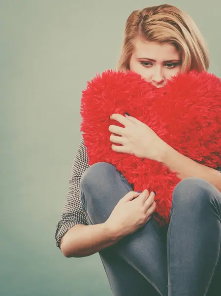 Mujer triste sosteniendo almohada roja en forma de corazón — Foto de Stock