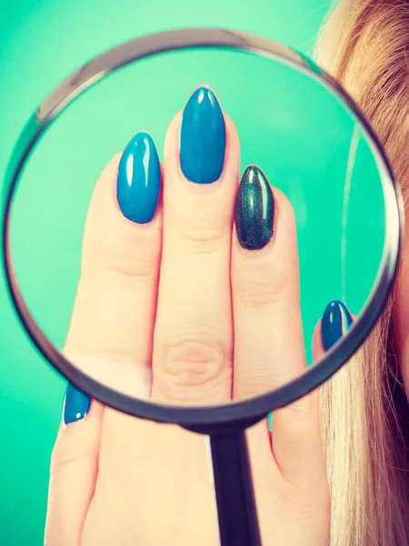 Женщина смотрит на ногти через увеличительное стекло — стоковое фото