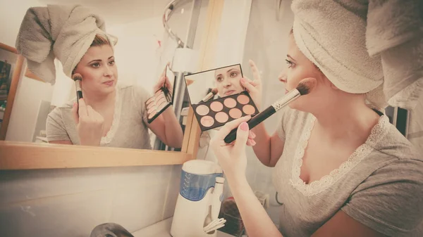 Woman in bathroom applying contour bronzer on brush