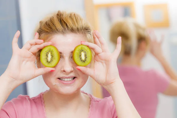 Vrouw met gel masker op het gezicht bedrijf kiwi — Stockfoto