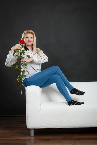 Κορίτσι που κάθεται στον καναπέ κρατά κόκκινο τριαντάφυλλο, στο σκοτάδι. — Φωτογραφία Αρχείου