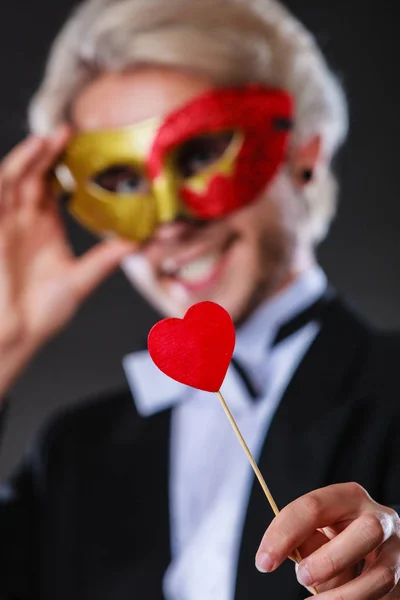 Man in carnival mask with heart stick love symbol