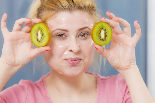 Vrouw met gel masker op het gezicht bedrijf kiwi — Stockfoto