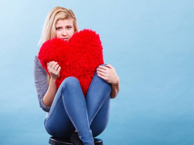 Kırmızı yastık kalp şeklinde tutan üzgün kadın