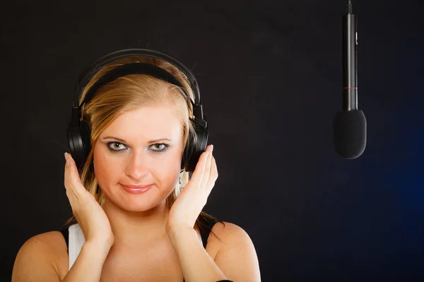 Woman singing to microphone wearing headphones in studio — Stock Photo, Image