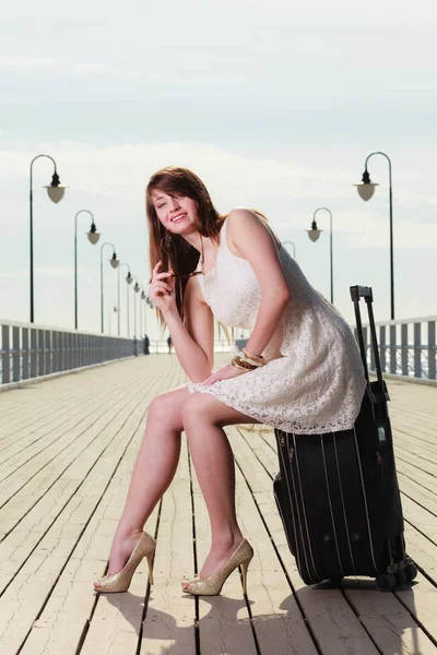 Woman sitting on suitcase, pier in background — Stock Photo, Image