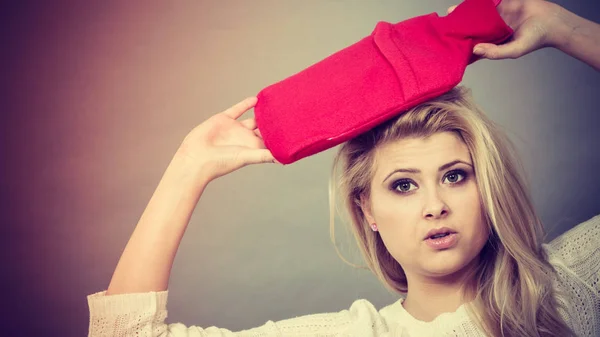 Woman holding red hot water bottle on head — Stock Photo, Image