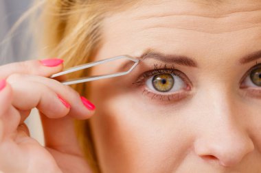 Kaşlarını cımbızla temizleyen kadın.