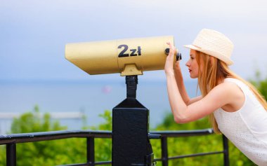 Teleskopla bakarak güneş şapkalı kadın turist