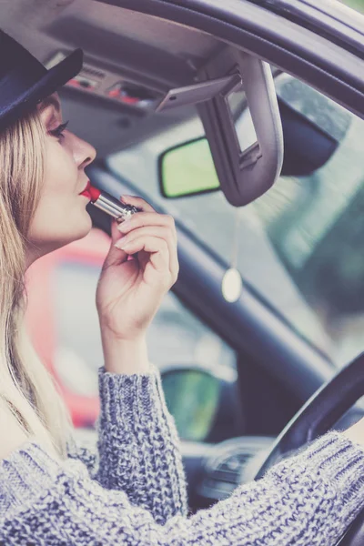 Mujer joven aplicando lápiz labial en el coche — Foto de Stock