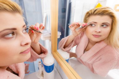 Kaşlarını cımbızla temizleyen kadın.