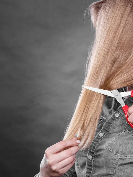 Blonde woman cutting her hair.