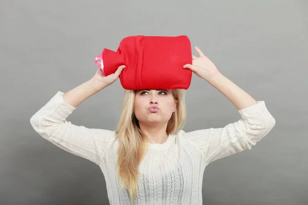 Woman holding red hot water bottle on head — Stock Photo, Image