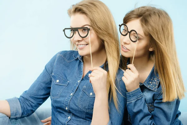 Två glada kvinnor innehar falska glasögon på pinne — Stockfoto