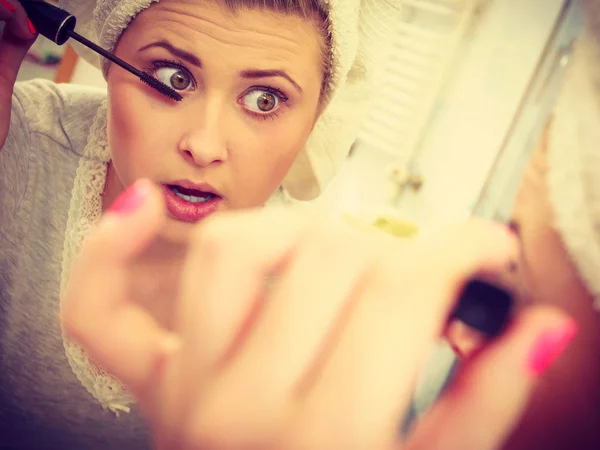 Woman in bathroom applying mascara on eyelashes Royalty Free Stock Images