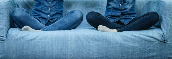 Two women wearing jeans sitting on sofa.